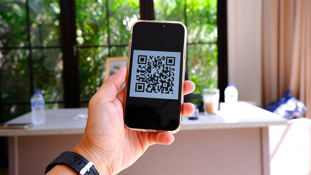 Hand holding smartphone with QR code on screen in an office room setting for digital payment or scanning