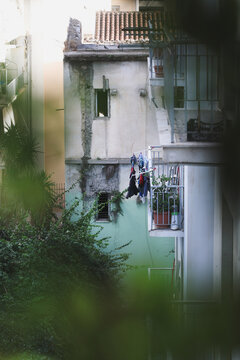 Weathered residential buildings in Athens with laundry hanging from a balcony, framed by lush greenery, revealing the textures and everyday character of the historic city.