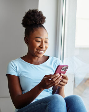 Portrait of a young black woman chatting with girlfriend at home, using modern mobile phone, checking social media, using mobile app, texting or browsing internet on his phone