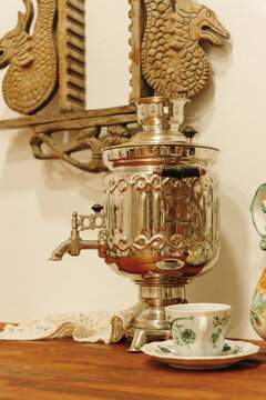 Vintage metal samovar displayed with a porcelain tea cup on a rustic wooden table. Traditional tea serving setup with classic decorative elements.