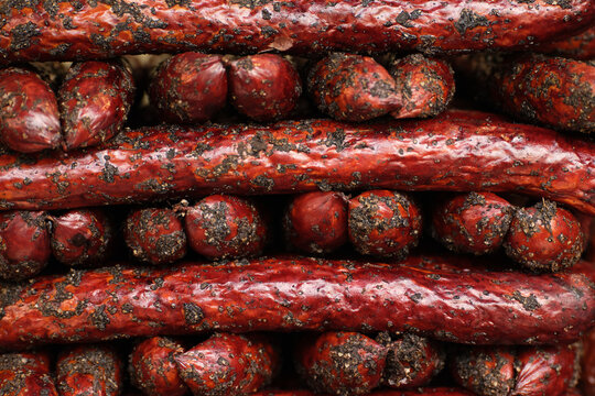 Macro full frame shot of dry cured smoked sausages and mini salami coated in black pepper and spices, tightly stacked in rows. Rich meat texture and food background pattern, ideal for butchery, charcu