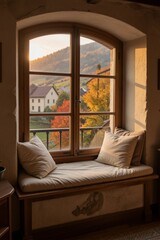 Fototapeta premium Warm autumn light pours through an arched wooden window in a cozy interior room, bathing a plush cushioned seat with a view of a rural landscape.
