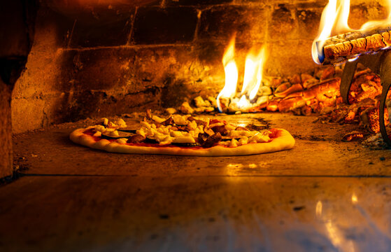 Italian pizza baking inside a traditional wood-fired brick oven with open flames