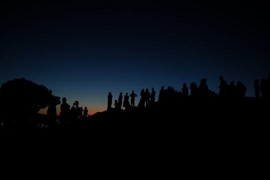 Silhouetted visitors gather on Areopagus Hill in Athens, Greece, at twilight, overlooking the city from the traditional site associated with the Apostle Paul's sermon.