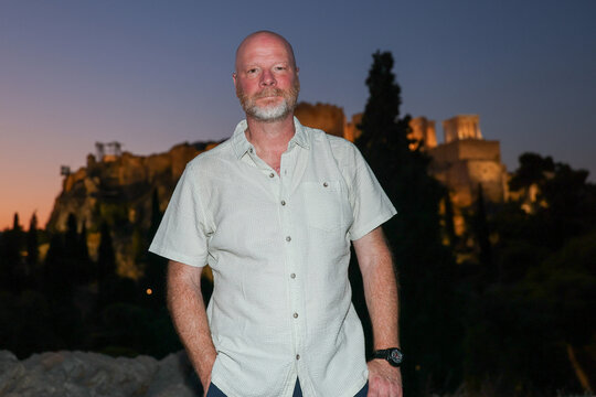 Portrait of a man with the illuminated Acropolis in Athens, Greece, in the background during twilight, combining a personal travel portrait with an iconic landmark.