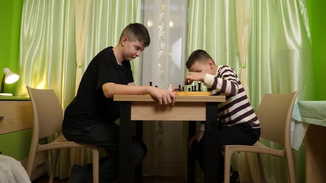 Two friends are playing chess at a table, taking turns making moves and enjoying spending time together at home