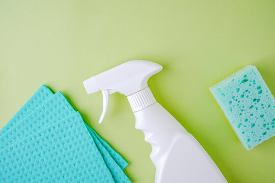 White spray bottle with cloths and sponge for cleaning on light green background