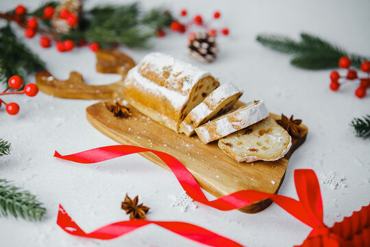 Classic Christmas Stollen sliced on wooden board with red ribbon and festive decor