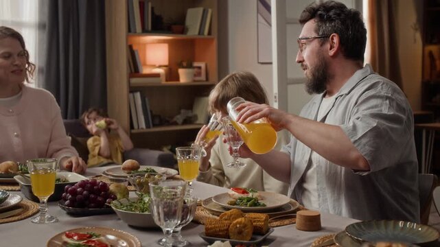 Caucasian father pouring orange juice for children during family dinner at home. Perfect for healthy beverage commercials or family lifestyle marketing campaigns