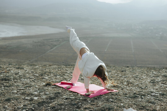 Woman practicing three legged downward facing dog yoga pose outdoors