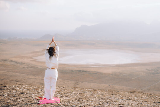 Back view of a woman meditating with raised arms in a vast landscape