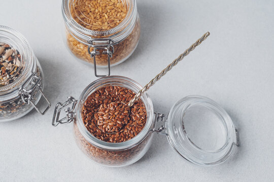Glass jars filled with flax seeds and other grains on a light background