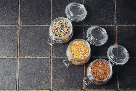 Three glass jars filled with assorted seeds on a dark tiled background