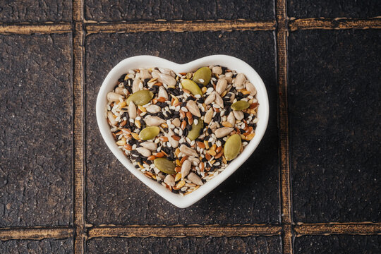 Heart shaped bowl filled with mixed seeds on a textured dark background