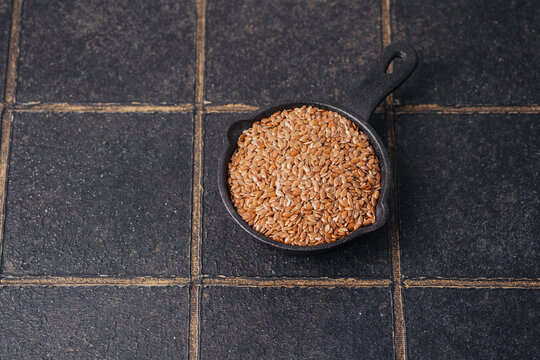Flax seeds in a small cast iron pan on a dark tiled background