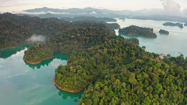 Aerial panorama of Cheow Lan Lake with numerous rainforest covered limestone islands rising from the turquoise waters under morning fog and clouds. Unique tropical landscape in Khao Sok National Park