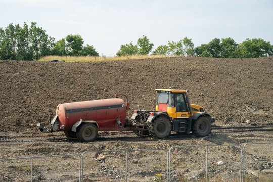 Tractor pulls red water tank across ploughed construction field