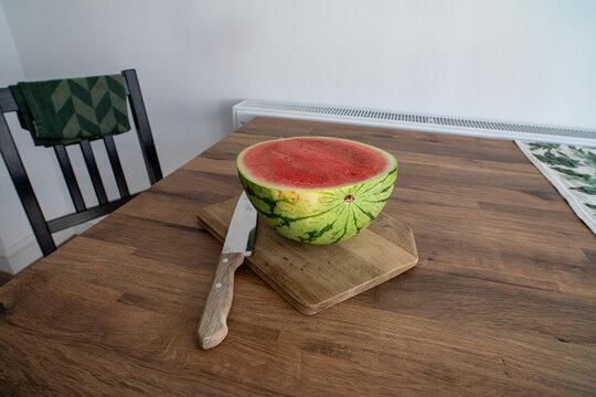 Halved watermelon on wooden cutting board with knife