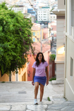 Woman walking up a historic street in Athens, Greece, with colorful buildings and the city rising in the background, capturing everyday life in the Greek capital.