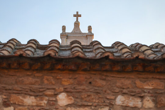 A Christian cross rises above a traditional tiled roof in Athens, Greece, highlighting the city's rich religious heritage and historic architecture.