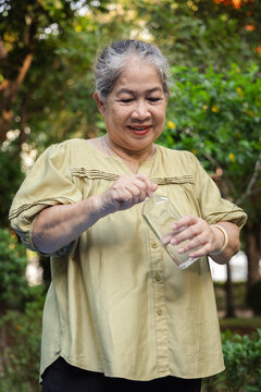 Asian senior woman opening drinking water bottle in green park in the evening, concept image for staying hydrated and healthy outdoors, front view portrait
