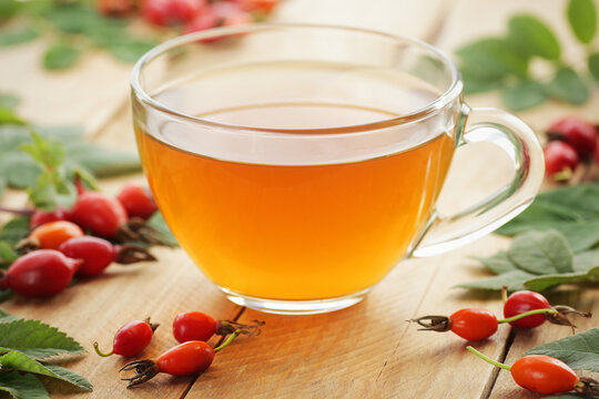 Healthy immune booster rosehip tea in a glass cup surrounded by red berries and leaves on a rustic wooden background