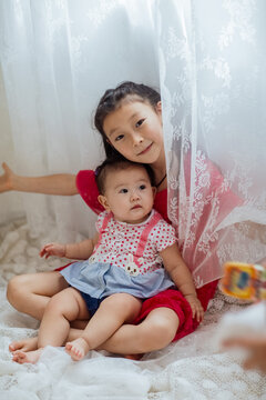 An Asian girl playing indoors with her baby.