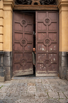 Smiling man Peeking From Vintage Wooden Doors in City