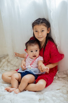 An Asian girl playing indoors with her baby.