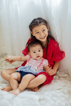 An Asian girl playing indoors with her baby.