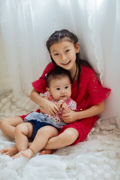 An Asian girl playing indoors with her baby.