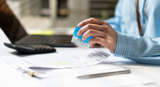 Close up of female business woman working at desk. Professional accountant hand using rubber stamp on paperwork, invoice or tax document. Financial validation, approval and accounting concept.