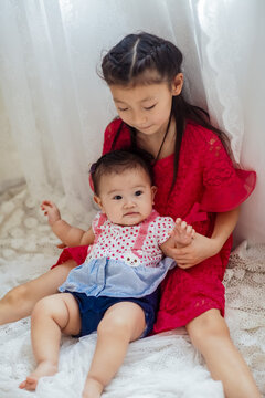 An Asian girl playing indoors with her baby.