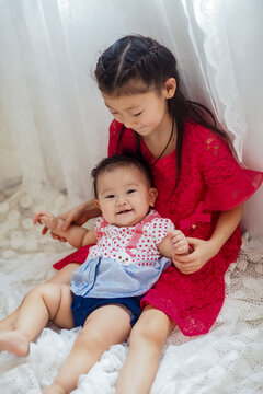 An Asian girl playing indoors with her baby.