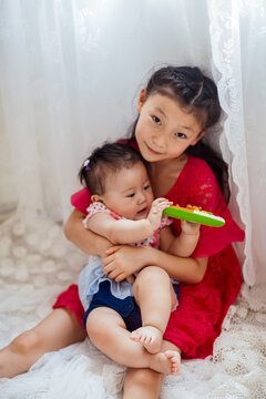An Asian girl playing indoors with her baby.