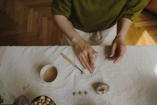 Female hands shaping clay with pottery tools in home studio.