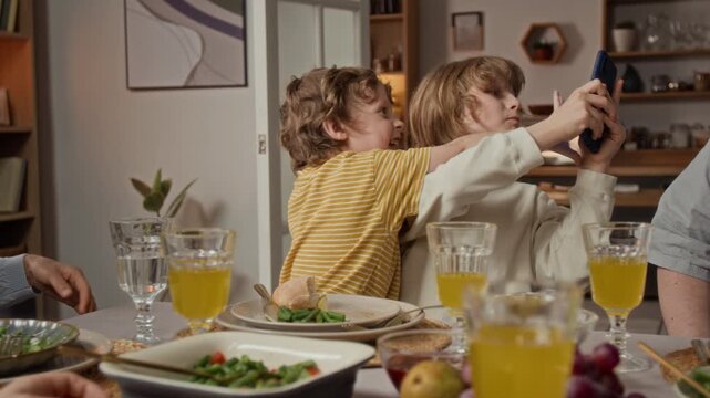 Caucasian teenager sitting at dinner table, using smartphone while younger brother playfully interrupting him. Footage for family lifestyle commercials and digital distraction concepts