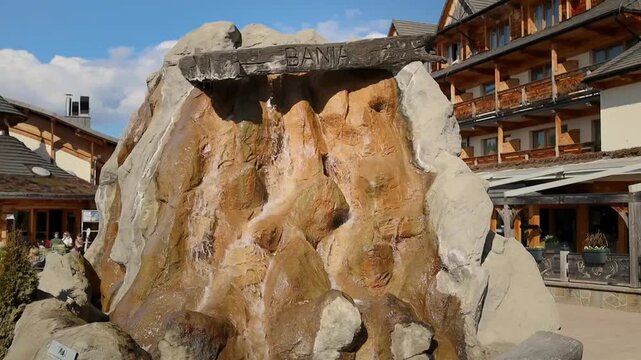 decorative artificial stone waterfall fountain with flowing water in the courtyard of a modern alpine style resort. Beautifully designed hotel territory featuring wooden chalet buildings, outdoor