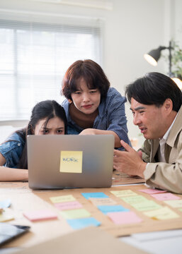 Three Asian business professionals huddled together, looking closely at a laptop screen to review important digital data and project updates.