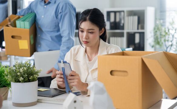 Depressed Asian businesswoman packing belongings into cardboard box after layoff in office