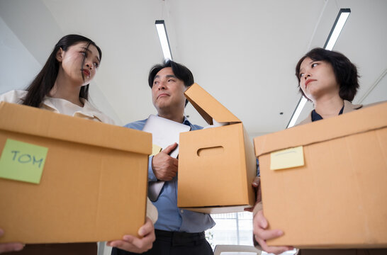 Sad Asian corporate team leaving office with cardboard boxes after mass layoff