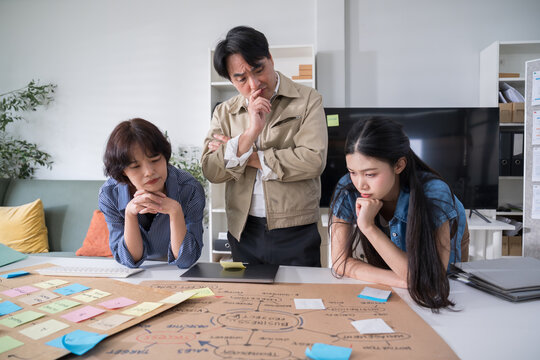 Focused Asian corporate team analyzing project details, looking seriously at a strategy map on the desk to find an effective business solution.