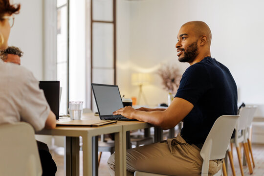 Man typing at laptop during meeting at bright office