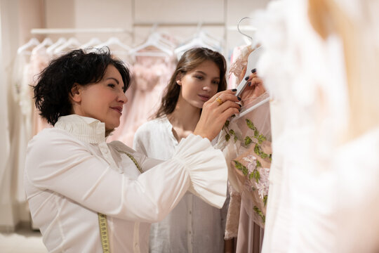 Female boutique owner assisting young woman and presenting dresses