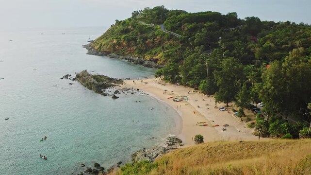 Nai Harn Beach, Phuket, Thailand. Tourists people relax on the sand, swimming in the clear blue water, and kayaking near the lush green coastline. Summer travel and relax. Aerial view drone shot