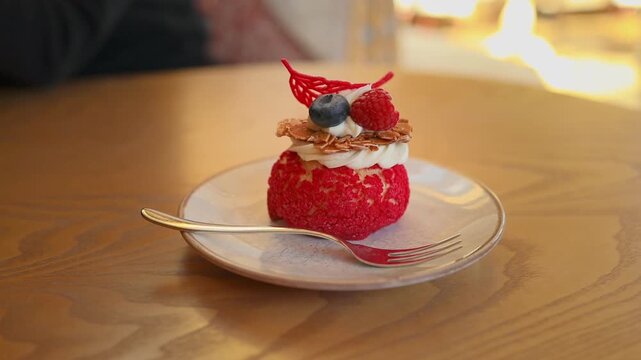 Close up view of a small delicious birthday cake or mini pavlova dessert topped with rich whipped cream, a fresh strawberry, and a blueberry. The pastry is elegantly served on a white plate on a