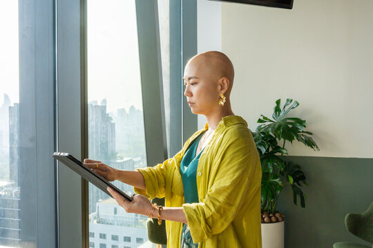 Woman Uses Tablet While Standing in Modern Office Near Window