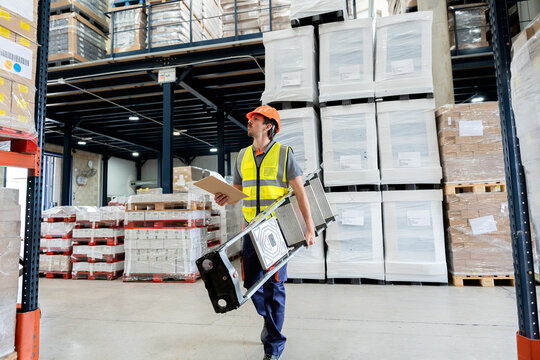 Warehouse worker carrying ladder checking inventory log