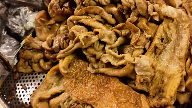 Close-up of cooked chicken feet and assorted chicken offal displayed for sale at a Thai street food market. Traditional Asian cuisine at a local food stall. 4K horizontal video.
