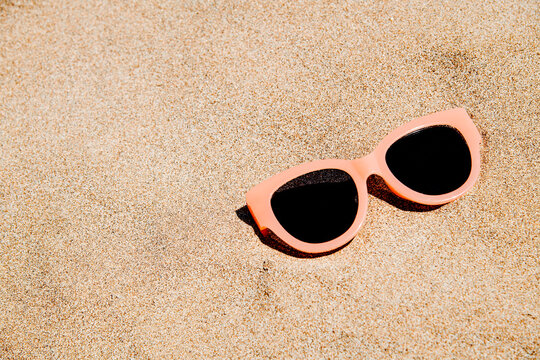 a pair of pale pink sunglasses on smooth beach sand